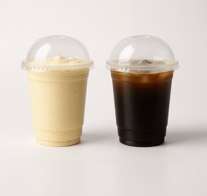 Two clear plastic cups with dome lids - one containing a creamy banana milkshake and the other containing dark cold coffee, both with condensation droplets on a white background